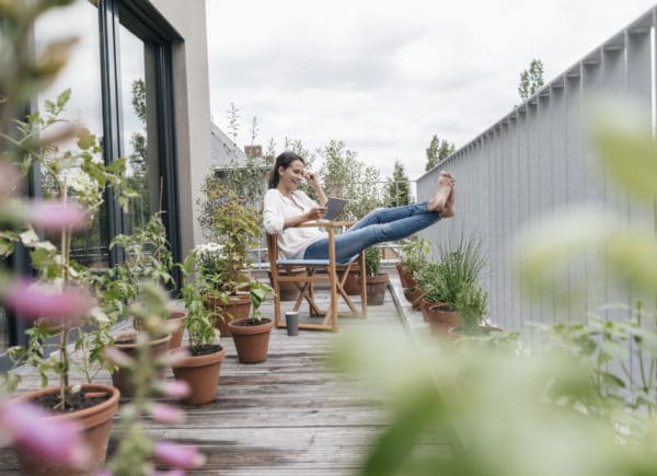 Young woman sitting outside on her porch watching videos on her tablet.