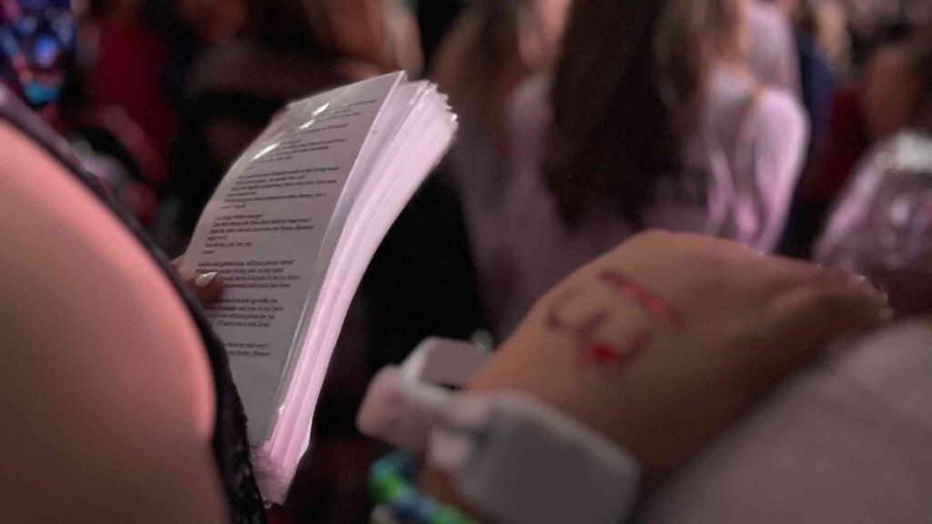 Teenager holding stack of laminated sheets of paper with Taylor Swift song lyrics at concert in Atlanta